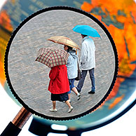 Tourists walking in the rain with umbrellas in summer seen through magnifying glass held against illuminated terrestrial globe